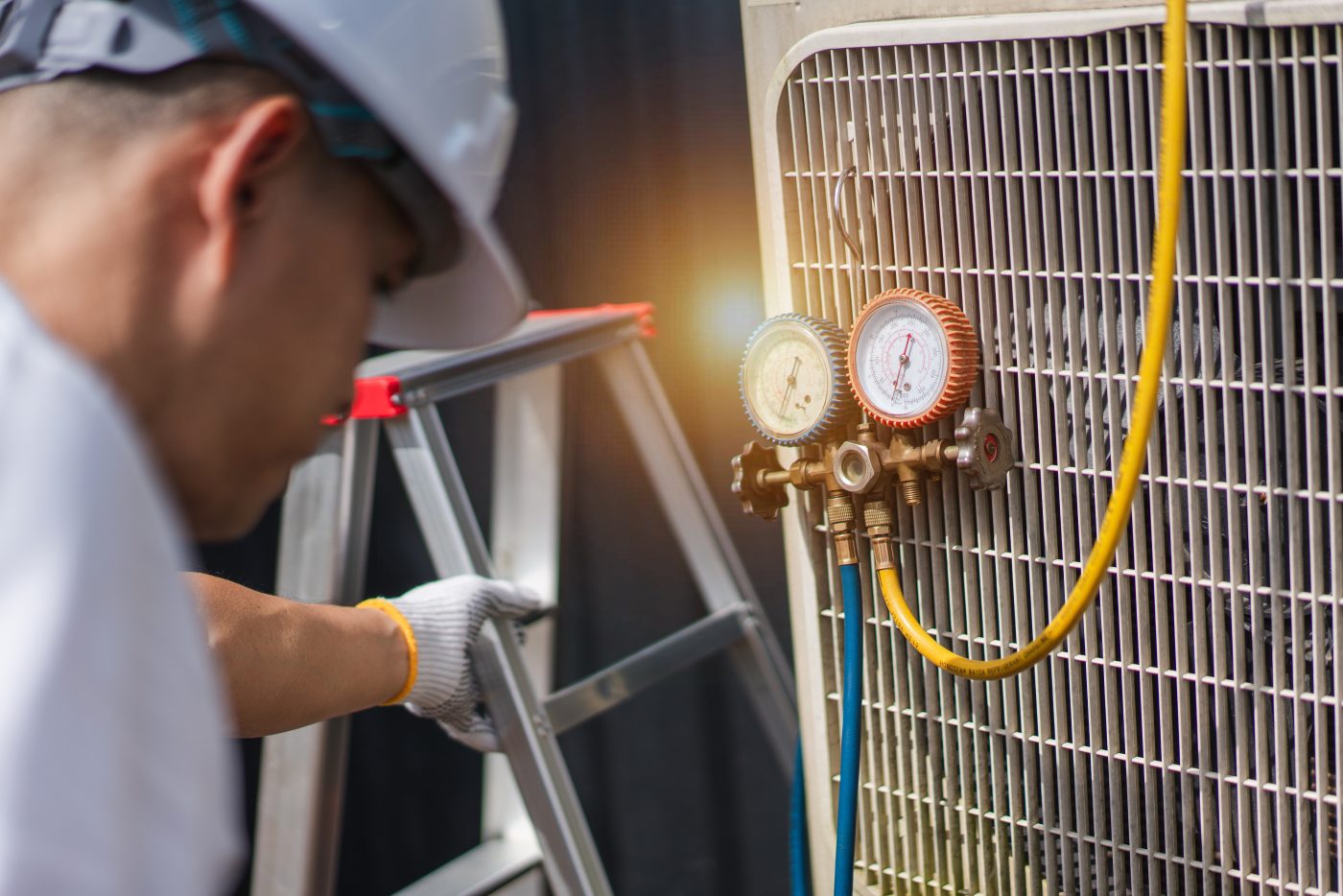 NCIS technician checking an air conditioner from a ladder.